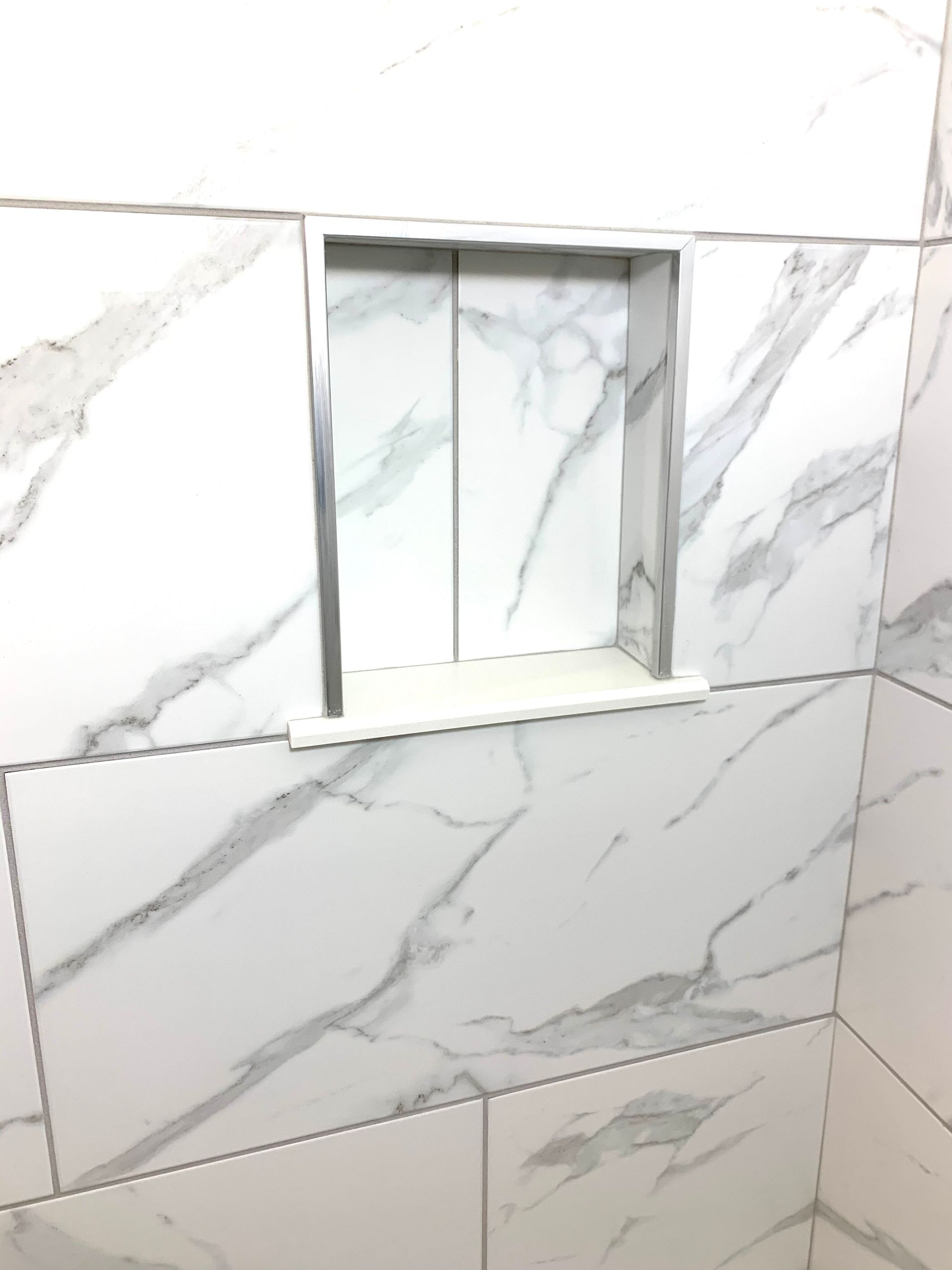 A bathroom with white marble tiles and shower niche