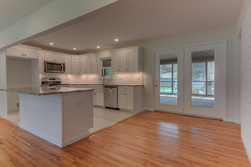 An empty kitchen with hardwood floors and white cabinets
