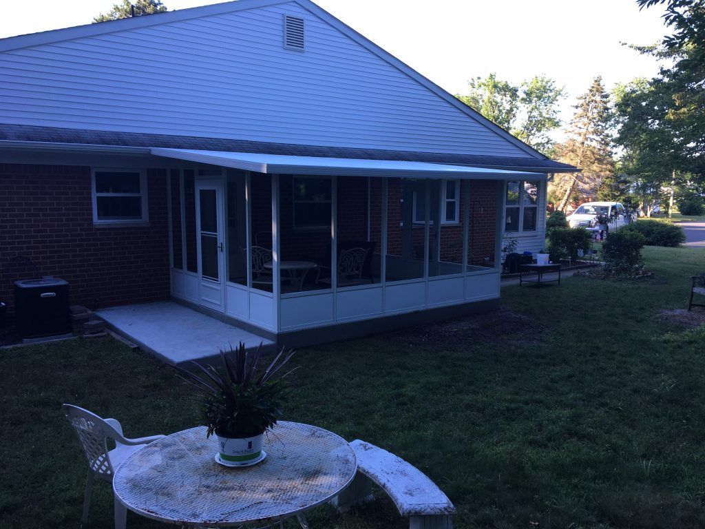 A screened-in porch with a table and chairs in front of a brick house