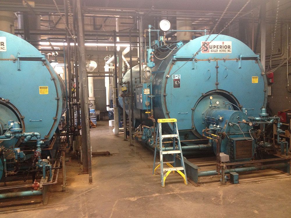 Two large blue industrial boilers in a machinery room, with pipes and a ladder nearby.