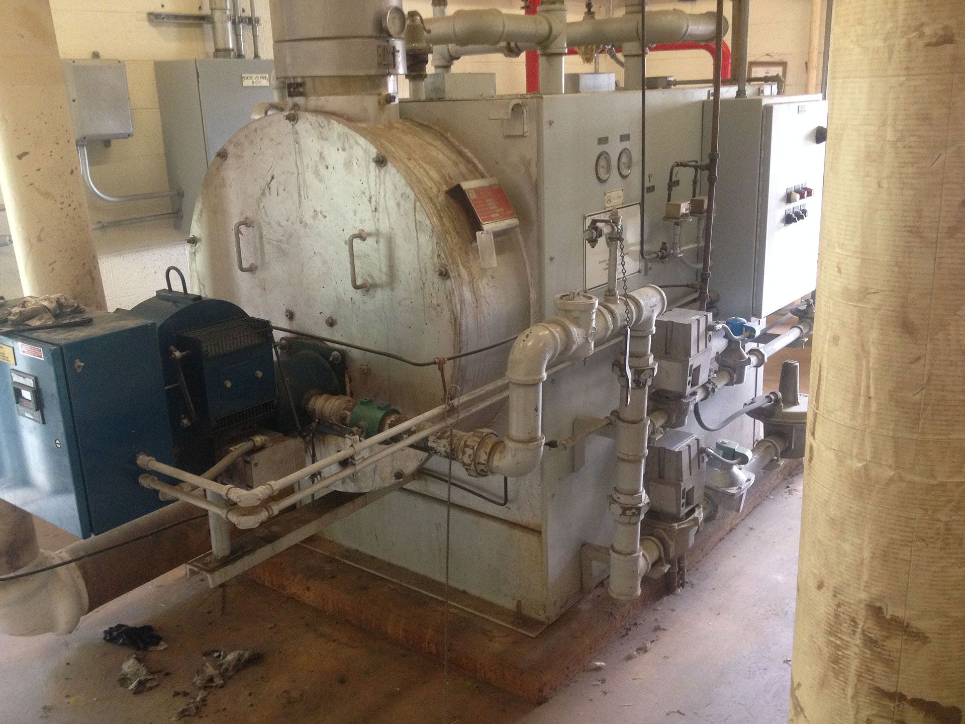 Large, industrial machine with pipes and electrical components in a concrete room.
