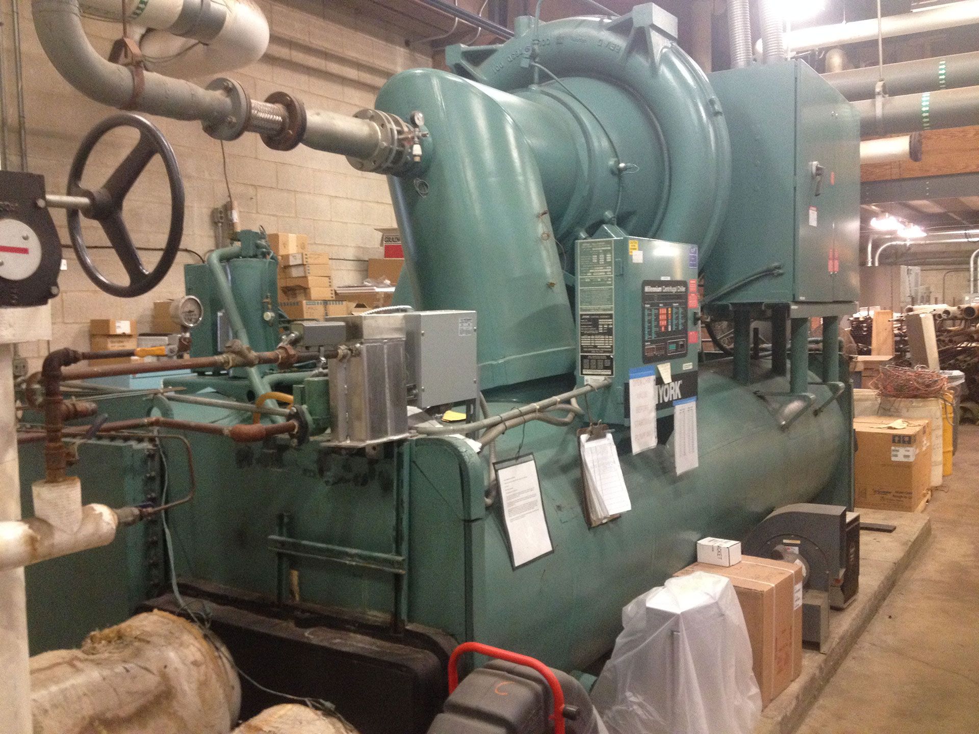 Large, teal industrial chiller in a mechanical room, with pipes, gauges, and electrical components.
