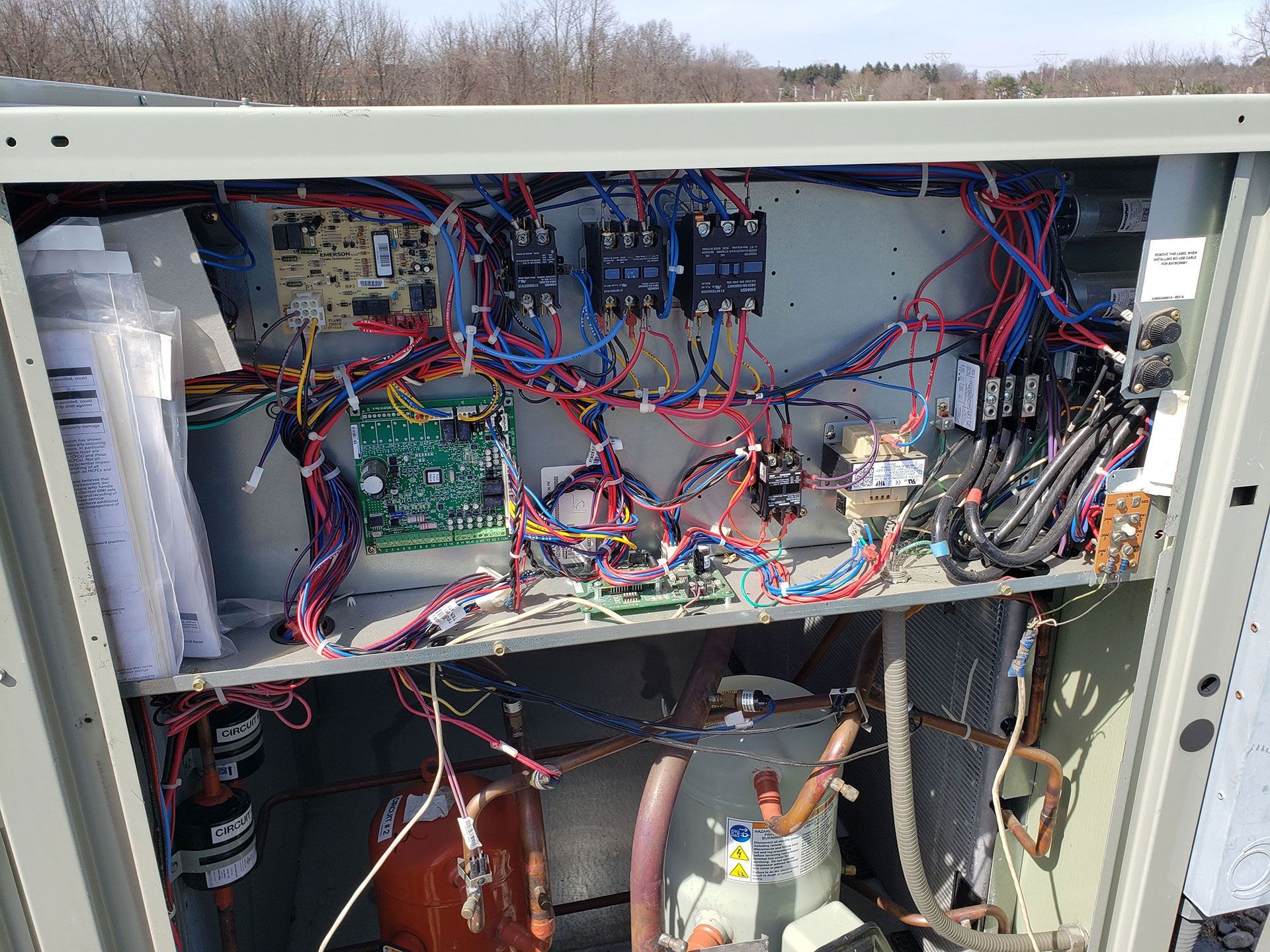 Open panel of HVAC unit with circuit boards, wiring, and other components.