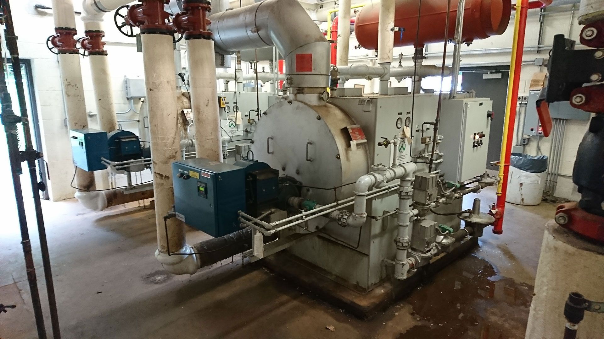 Industrial machinery in a mechanical room with pipes, valves, and control panels.