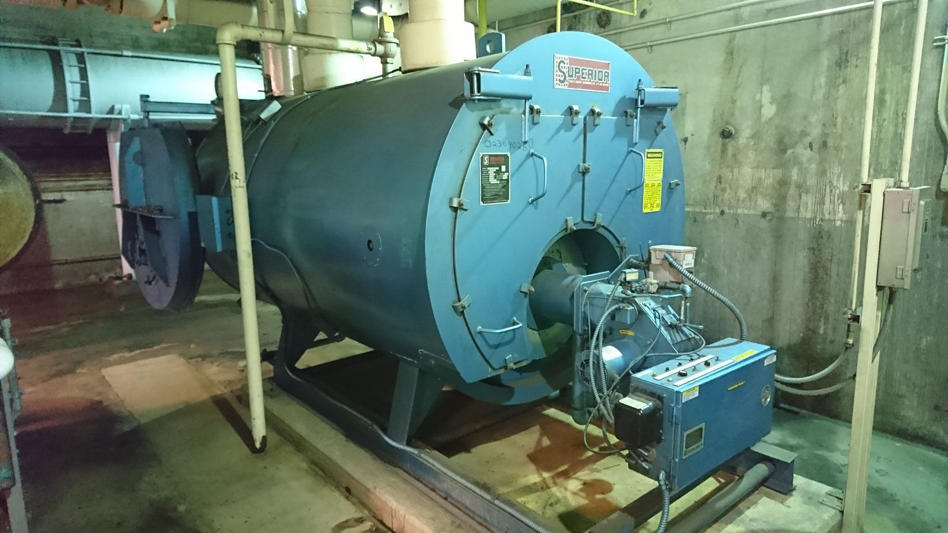 Blue industrial boiler in an equipment room, with attached components and piping.