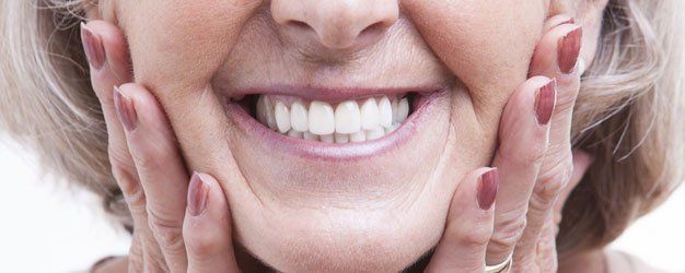 Smiling person touching their cheeks with manicured hands, showing bright white teeth