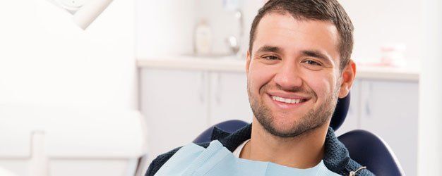 Smiling dentist in a chair with a light blue bib in a bright office