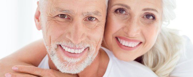 Smiling couple with gray hair embracing against a white background