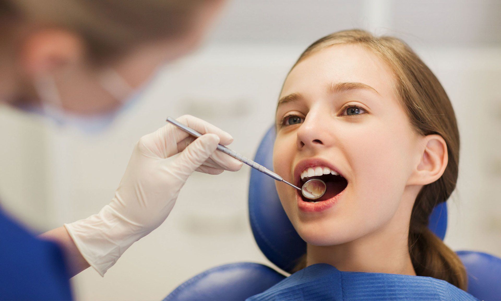 Dentist examining a patient’s open mouth with a dental mirror in a clinic
