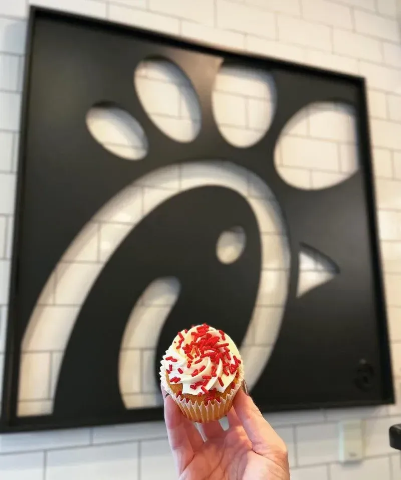 Hand holding a cupcake with red and white frosting in front of a Chick-fil-A sign