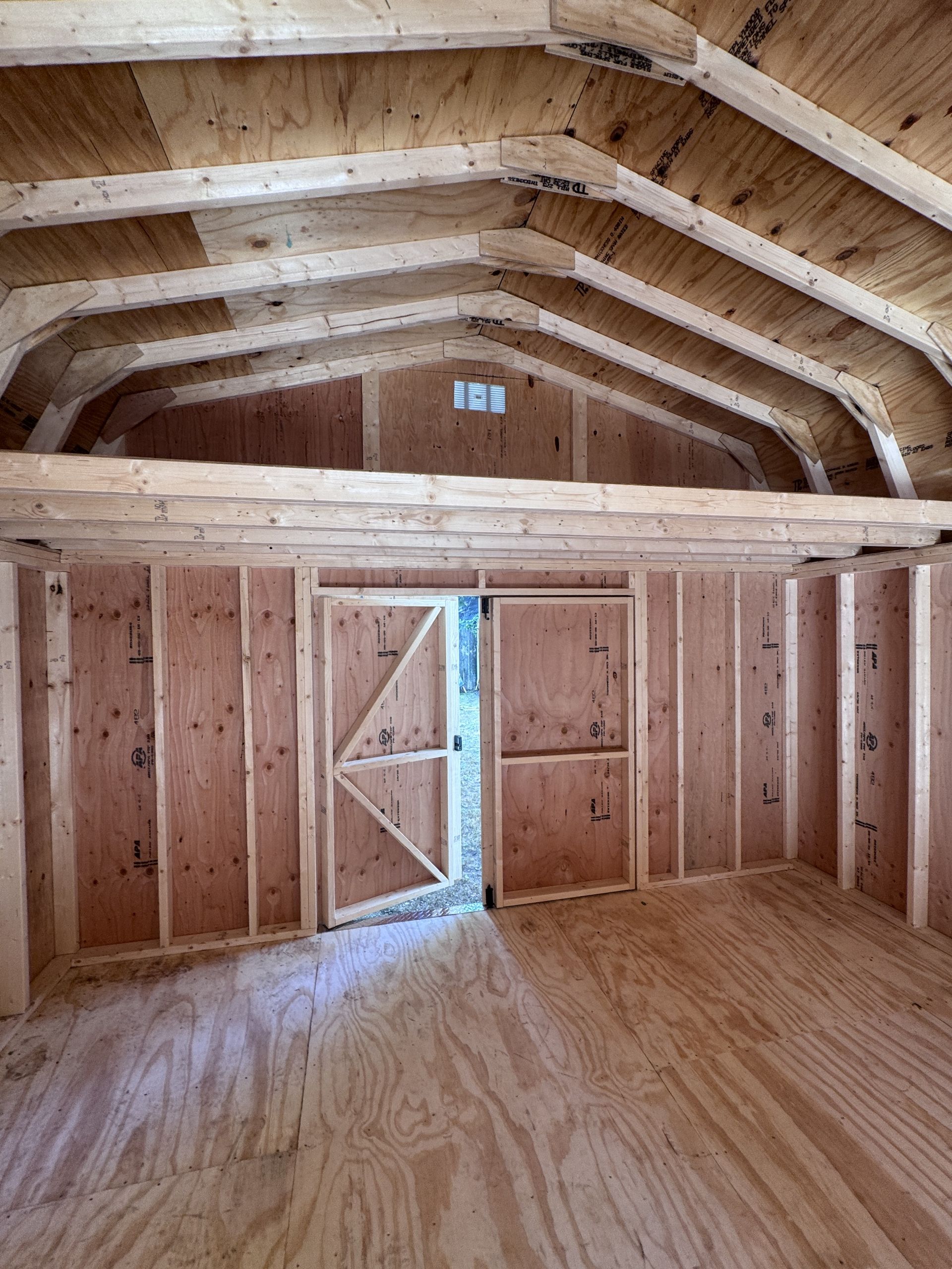 Unfinished wooden barn interior with exposed rafters and a partially open double door letting in daylight