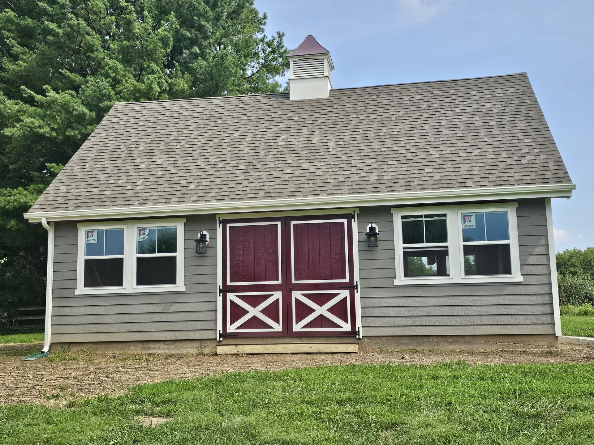 Small gray shed with red double doors and a wavy shingled roof, set in a grassy yard.