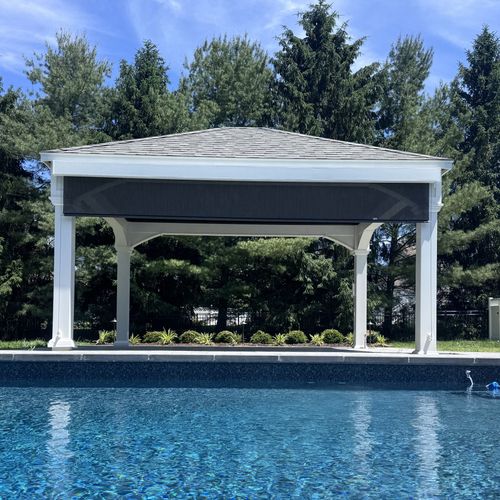 White gazebo by a blue swimming pool with trees and clear sky in the background