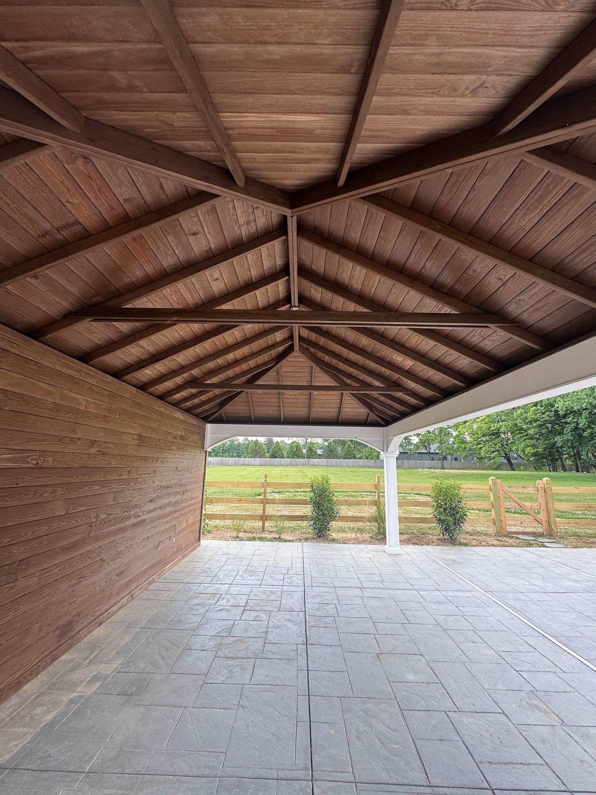 Open-sided rustic pavilion with a tiled floor and thatched roof overlooking a field