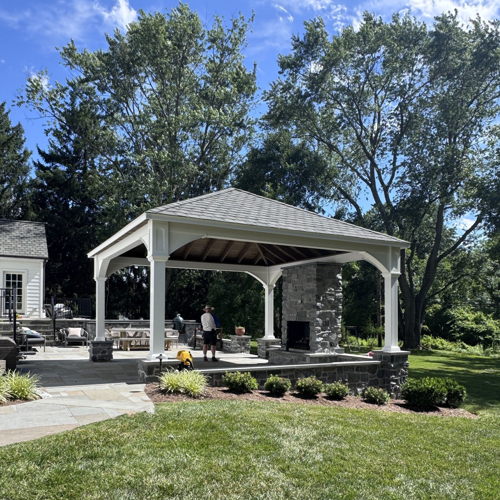 Stone gazebo in a sunny landscaped park with a person standing inside and trees in the background