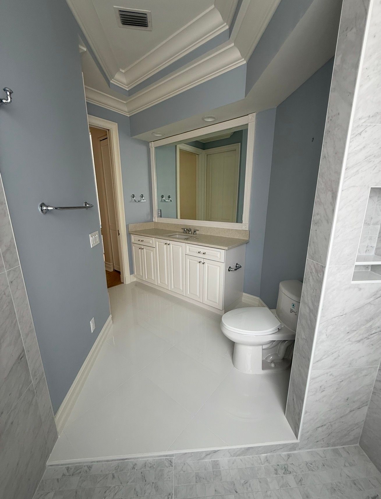 Small bathroom with gray walls, white toilet, sink vanity, and large mirror in a narrow space
