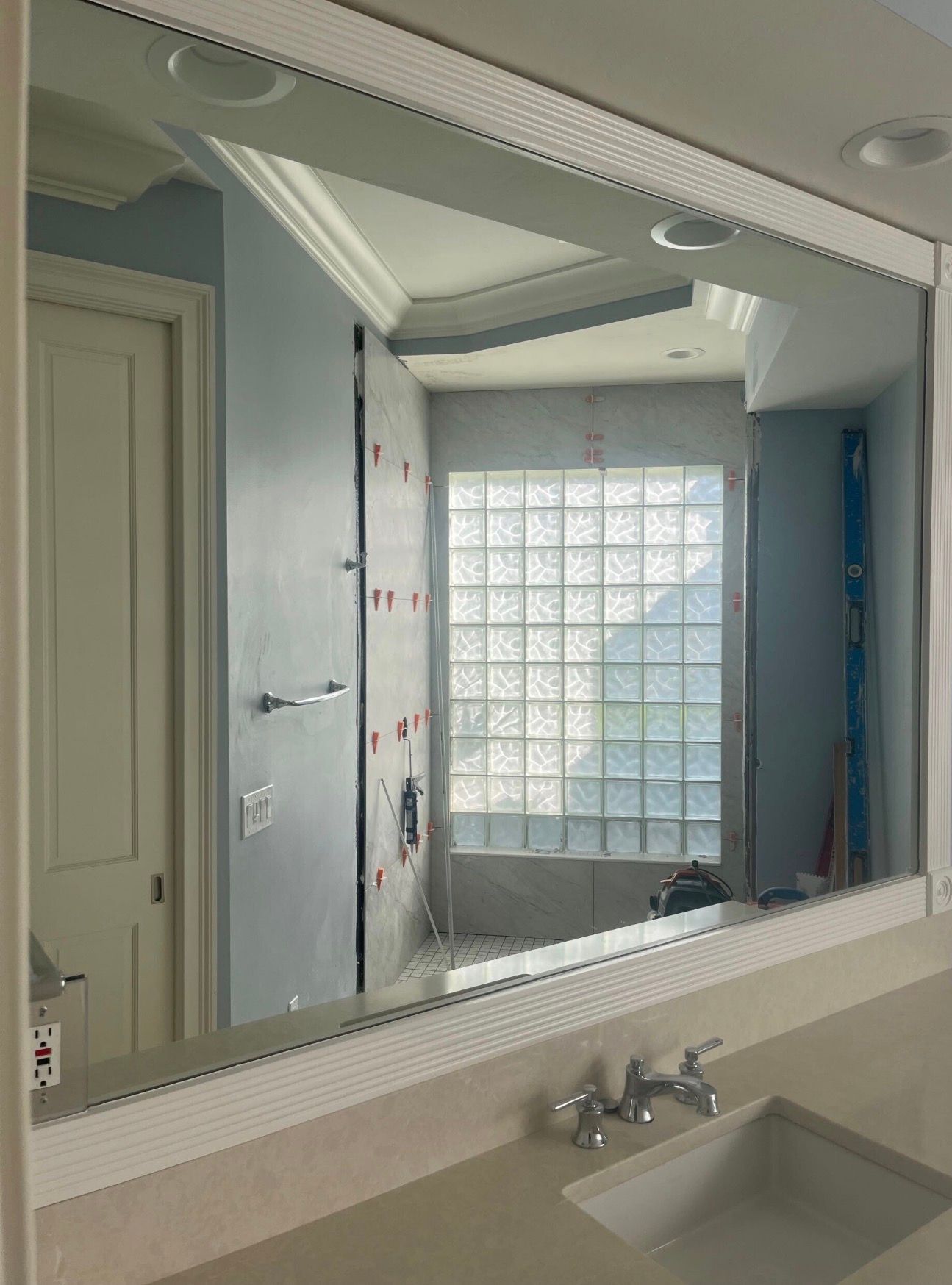 Bathroom mirror view of a modern interior with sink, cabinet, recessed lights, and glass block window.