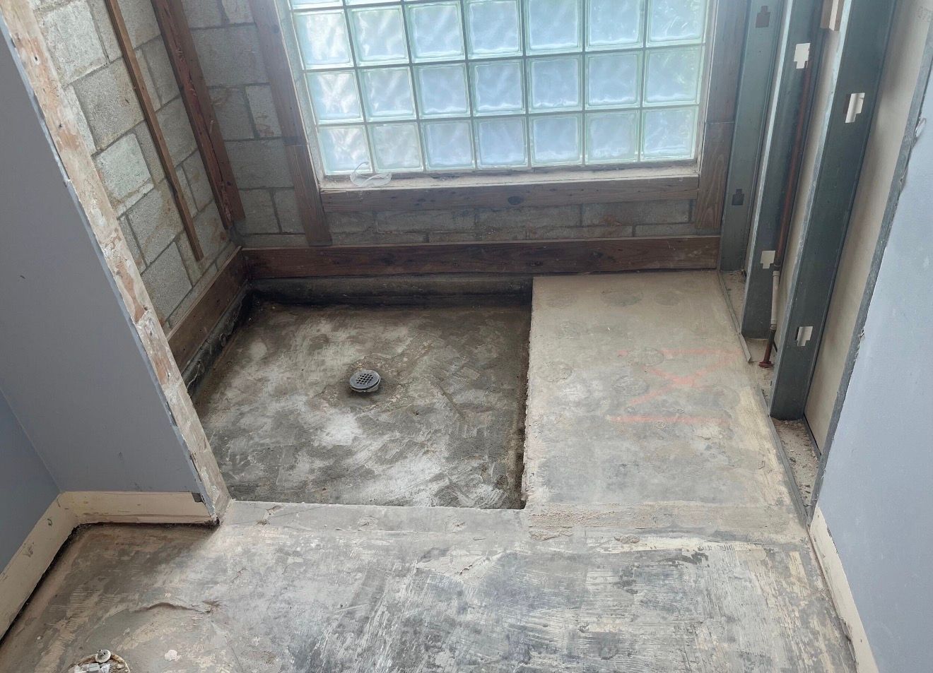 Small bathroom with a concrete floor, exposed walls, and a glass-block window at the end.