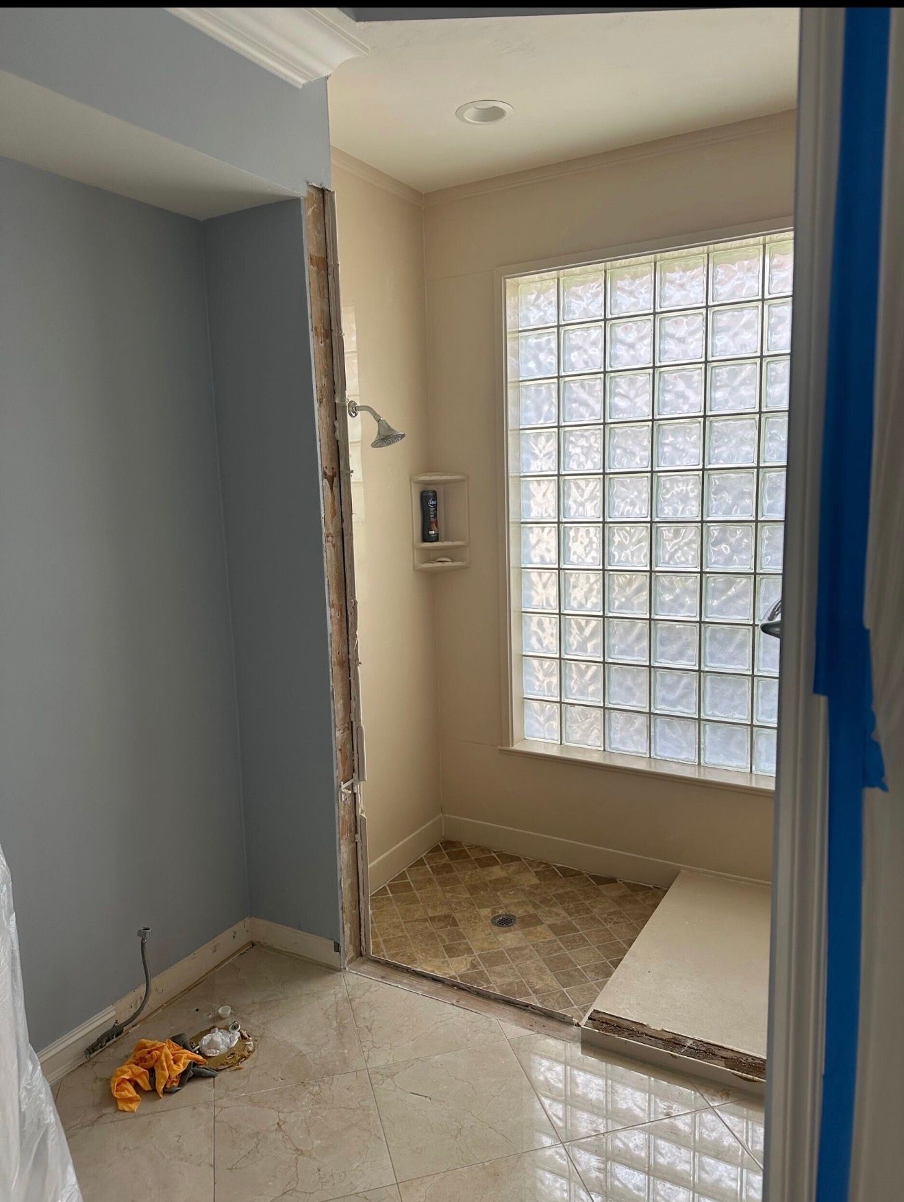 Small bathroom under renovation with glass block window, tiled shower floor, and blue walls.