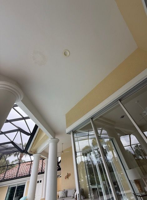 Covered patio with white ceiling, columns, and glass sliding doors beside a house