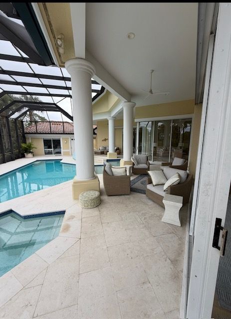 Covered poolside patio with white columns, wicker seating, and a view of the pool and screened lanai