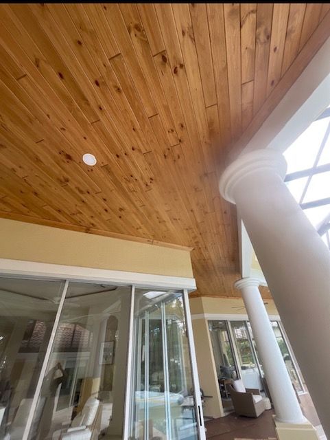 Covered porch with wood ceiling, white columns, glass doors, and a cushioned chair seating area.