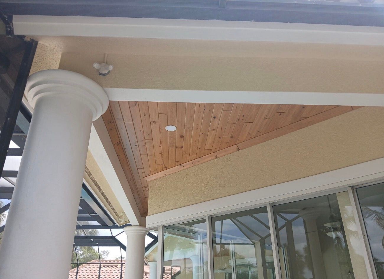 Covered outdoor walkway with white columns, wood-paneled ceiling, and glass windows