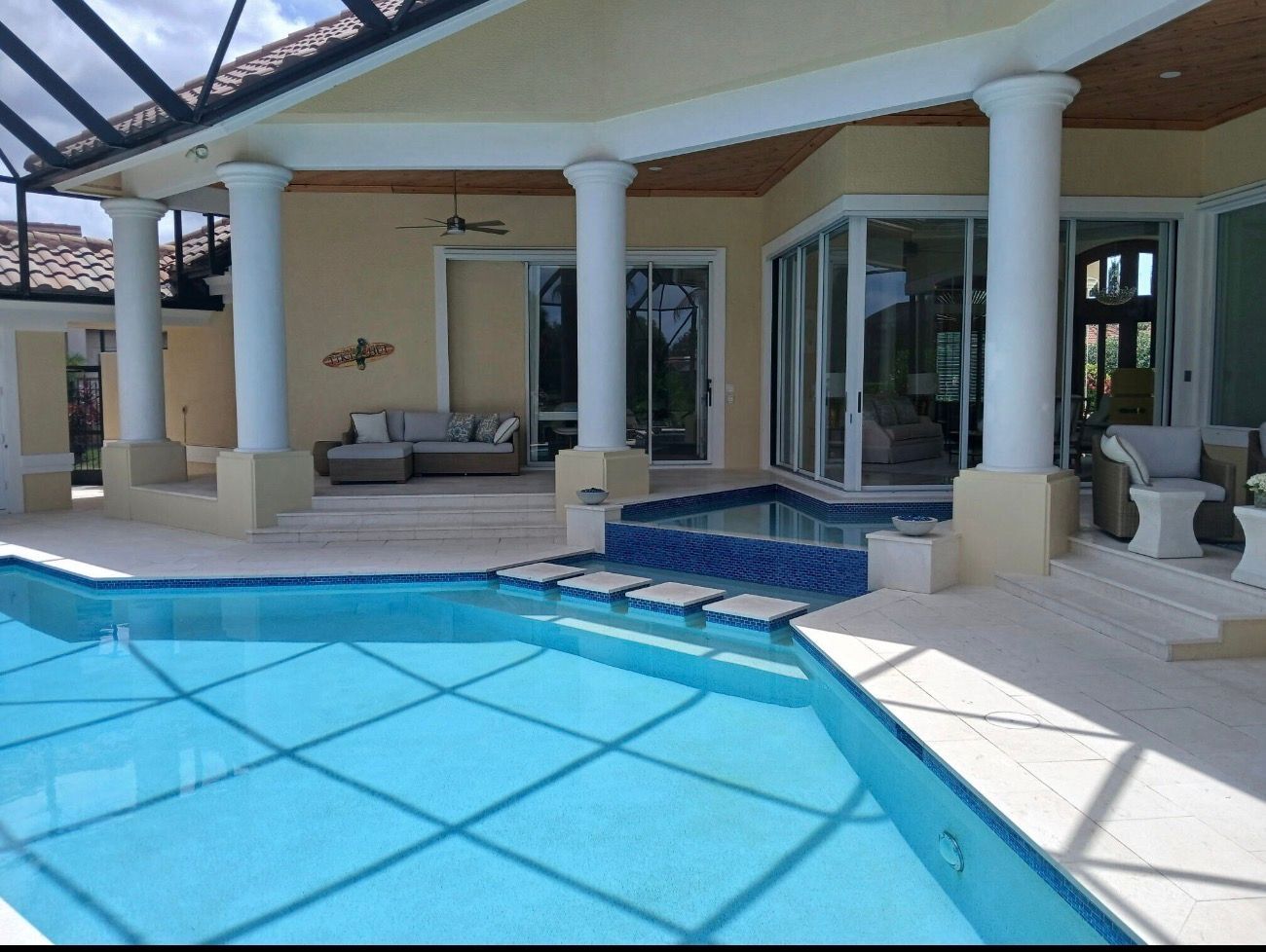Poolside patio with blue water, white columns, and outdoor seating under a covered lanai