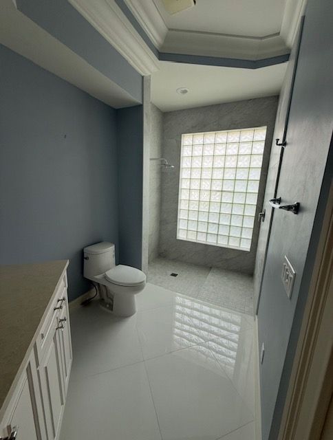 Empty bathroom with white tile, toilet, vanity, and glass-block window letting in light.