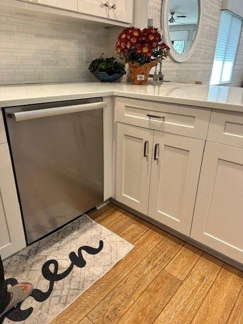 Stainless steel dishwasher and white cabinets in a kitchen, next to wooden flooring.