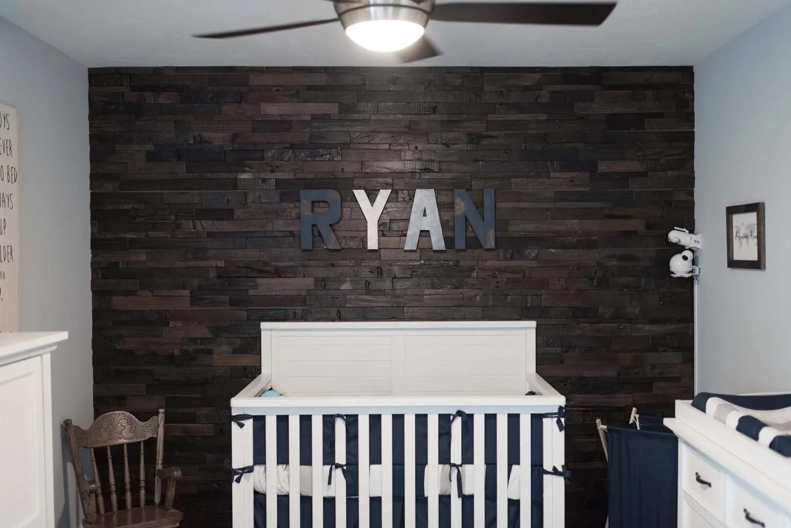 Nursery with dark wood accent wall, crib, and name 