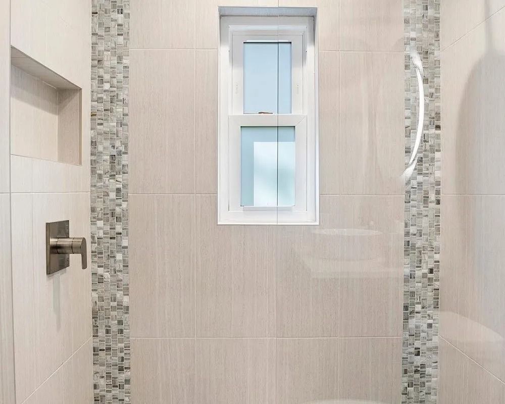 Shower interior with tiled walls, small window, and mosaic accents.
