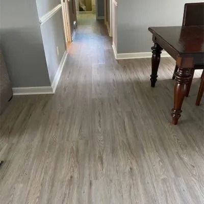 A dining room with gray walls and light wood-look flooring. A dark wooden table sits on the right.