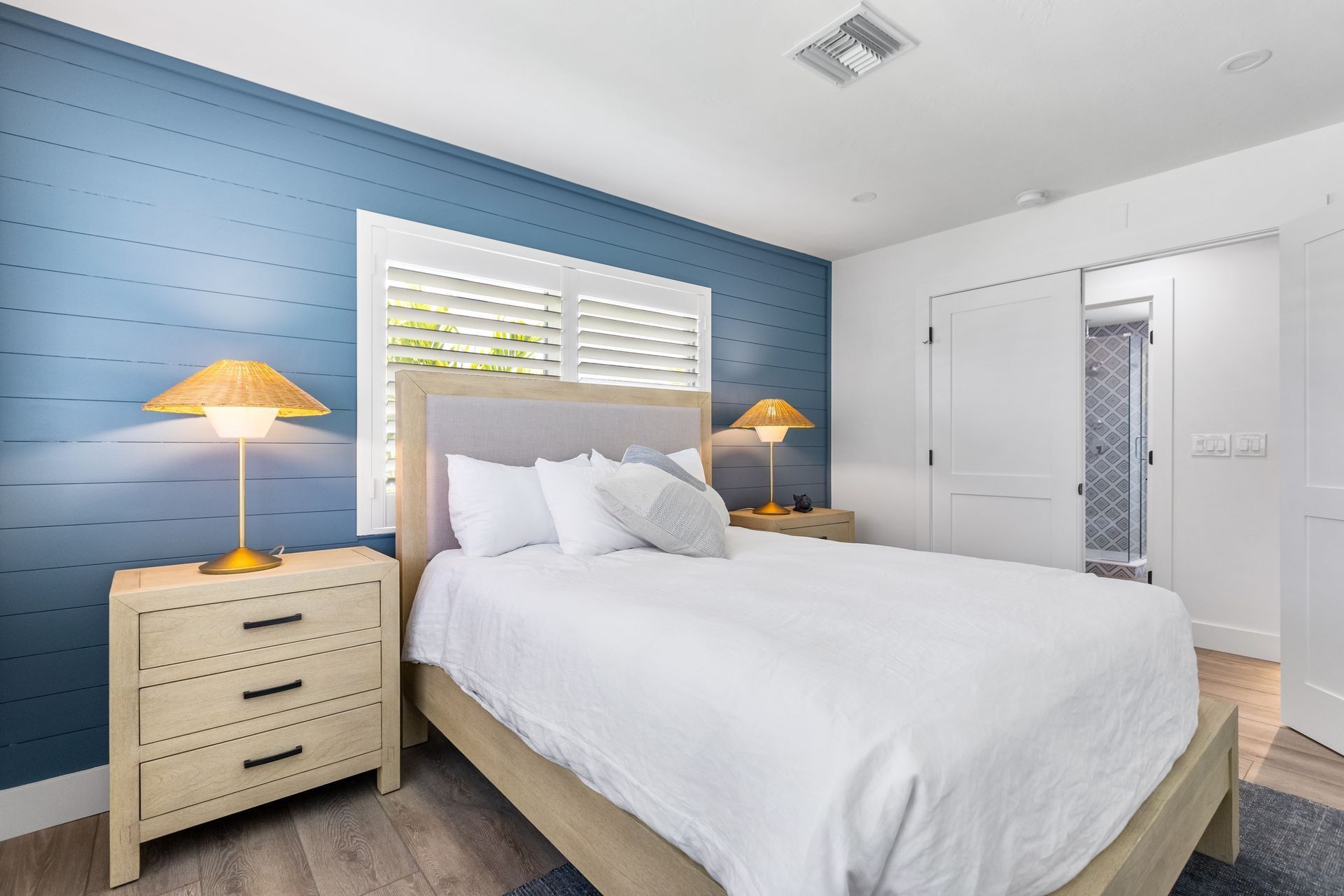 Bedroom with blue accent wall, white bedding, wooden nightstands, and window with shutters.