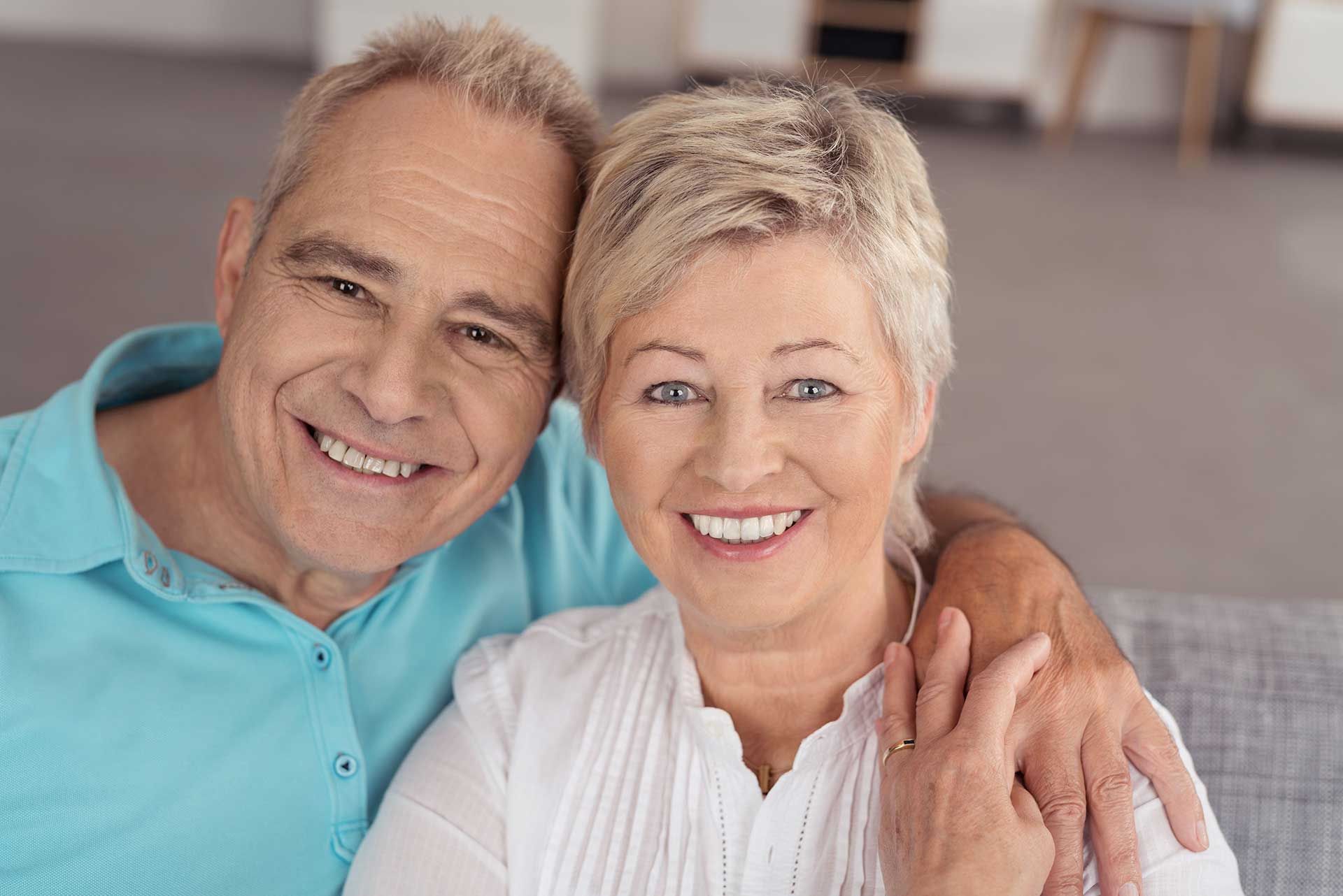 Smiling couple in light blue and white shirts, embracing against a soft gray background