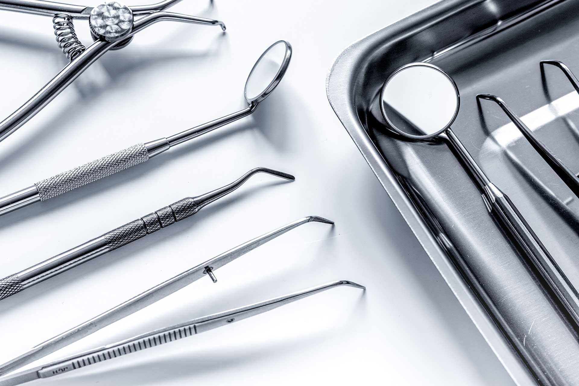 Assorted silver dental tools and mirrors arranged on a white surface, with a tray at right