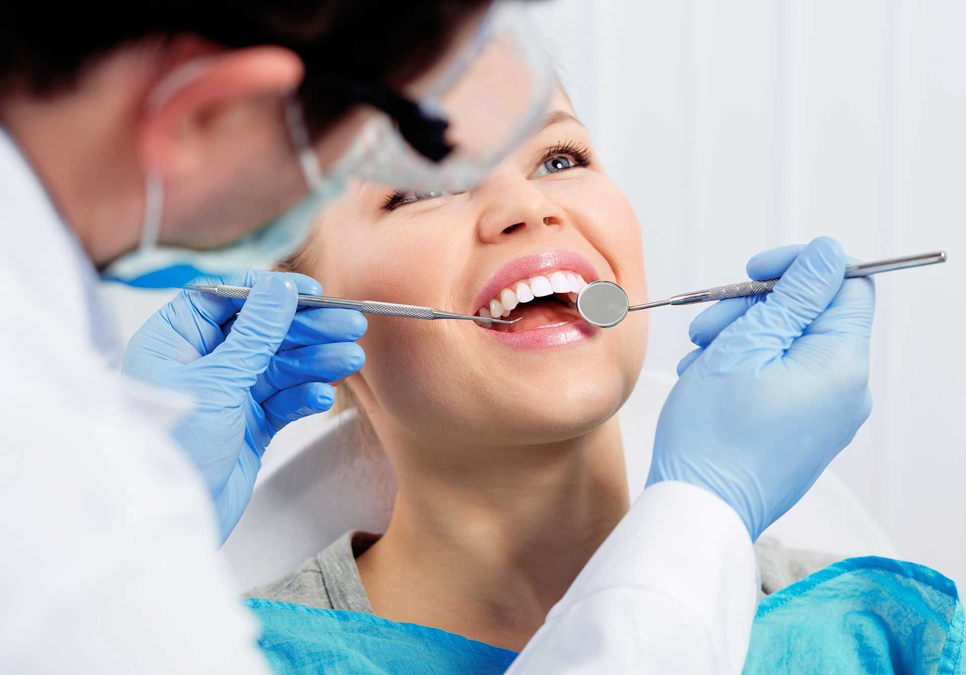 Dentist examining a smiling patient’s teeth with a dental mirror and tool in a bright clinic