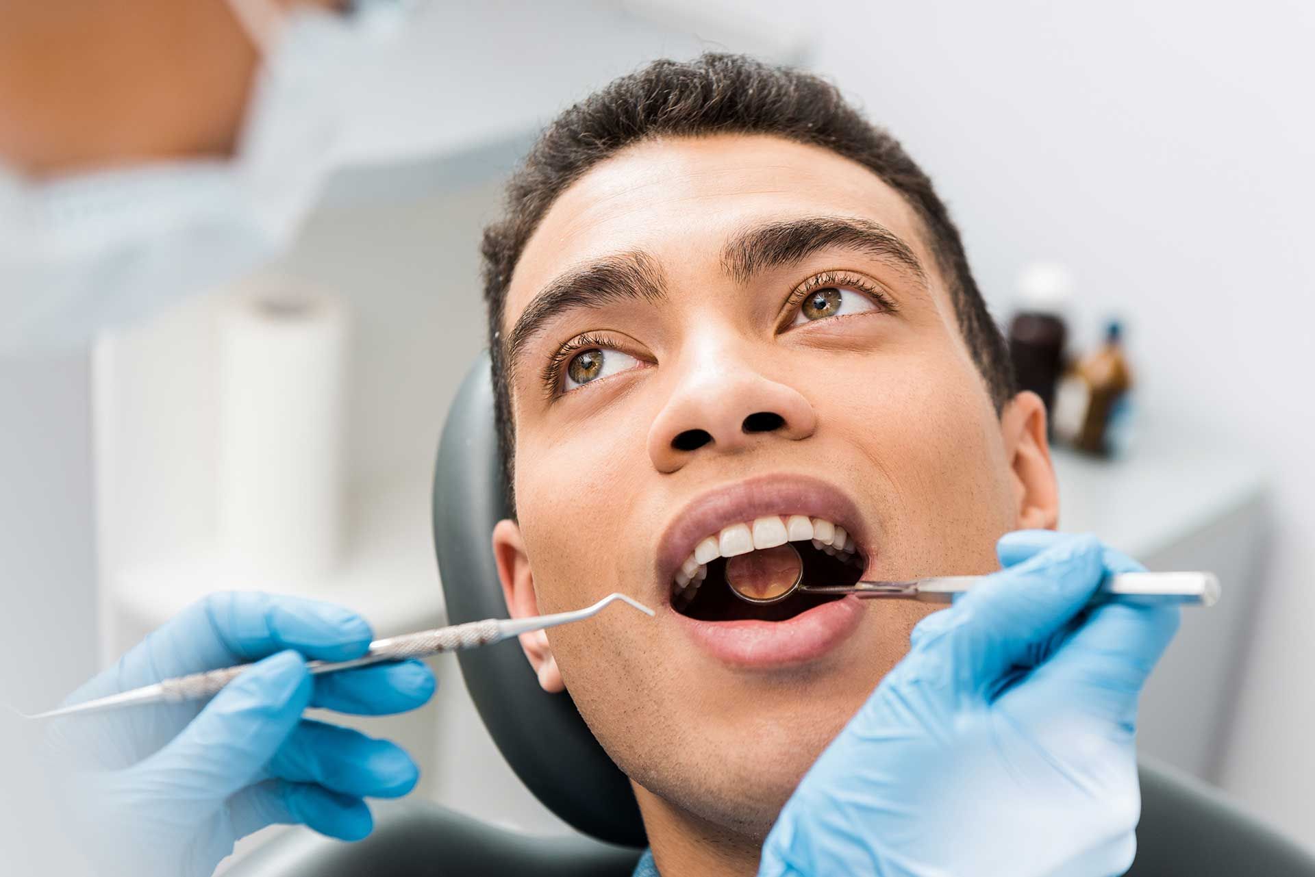 Patient with open mouth during a dental exam while gloved hands use dental tools in a clinic