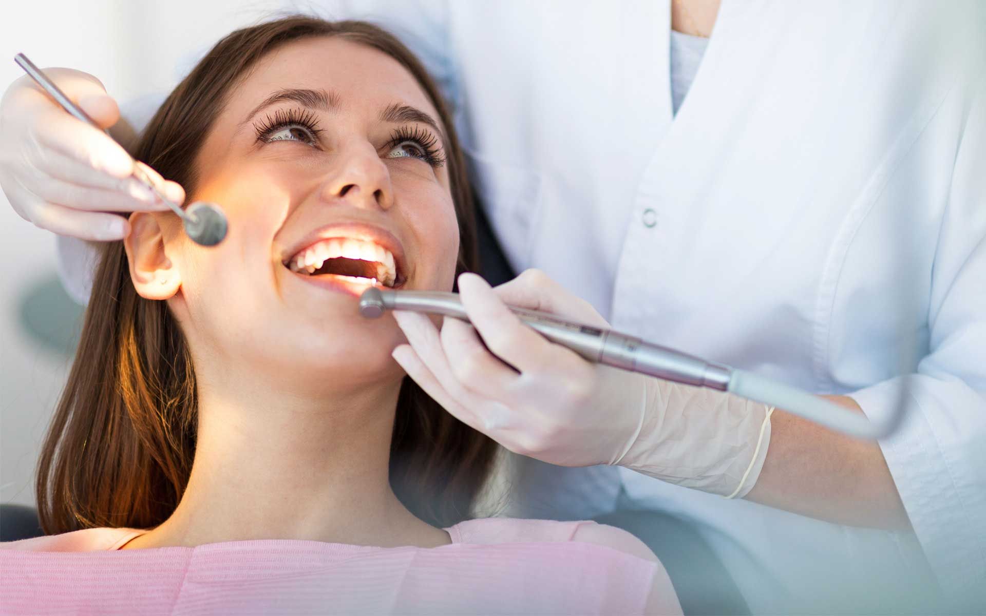 Dentist examining a smiling patient’s teeth with dental tools and gloves