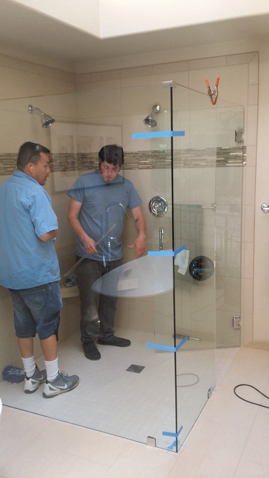 Two men are working on a glass shower door in a bathroom.