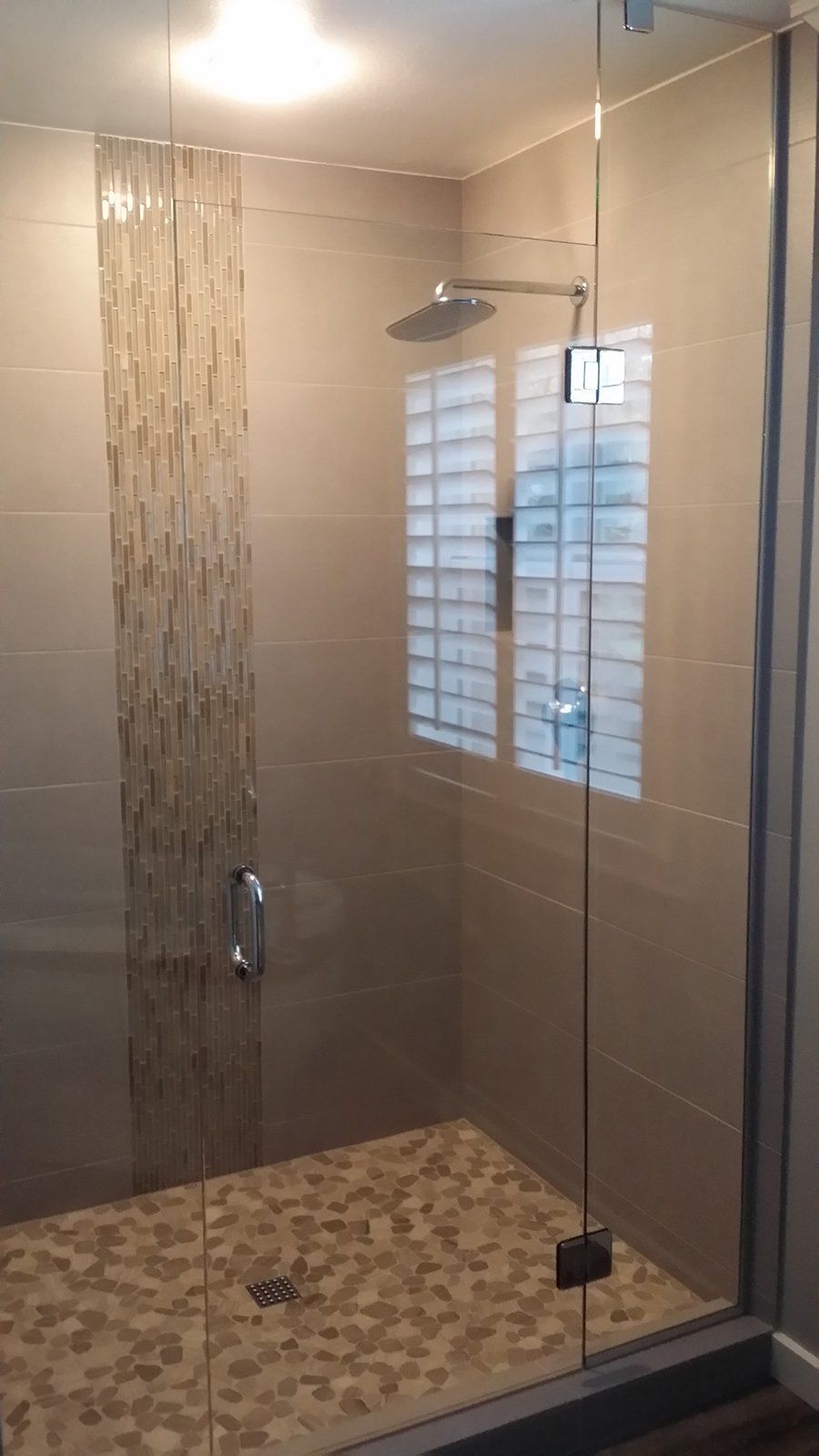 A walk in shower with a glass door and a window.