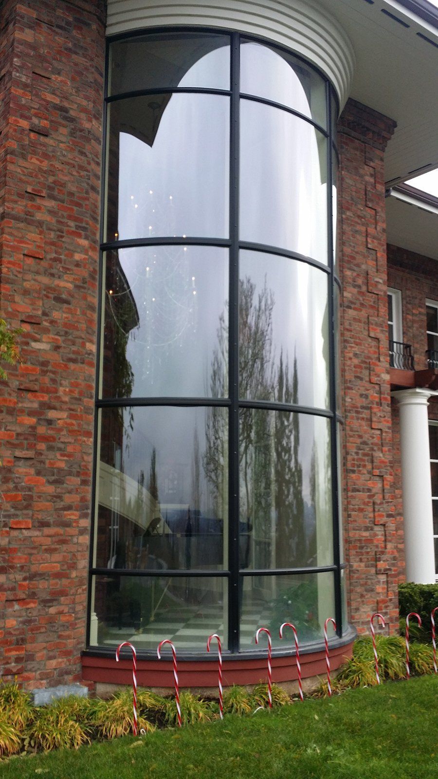 A large curved window on the side of a brick building with candy canes in front of it.