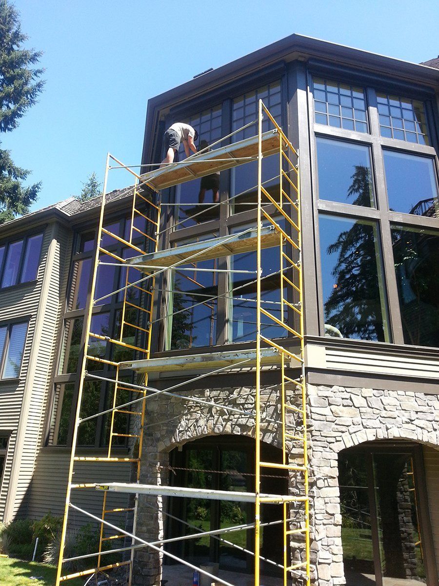 A man is standing on a scaffolding in front of a large house.