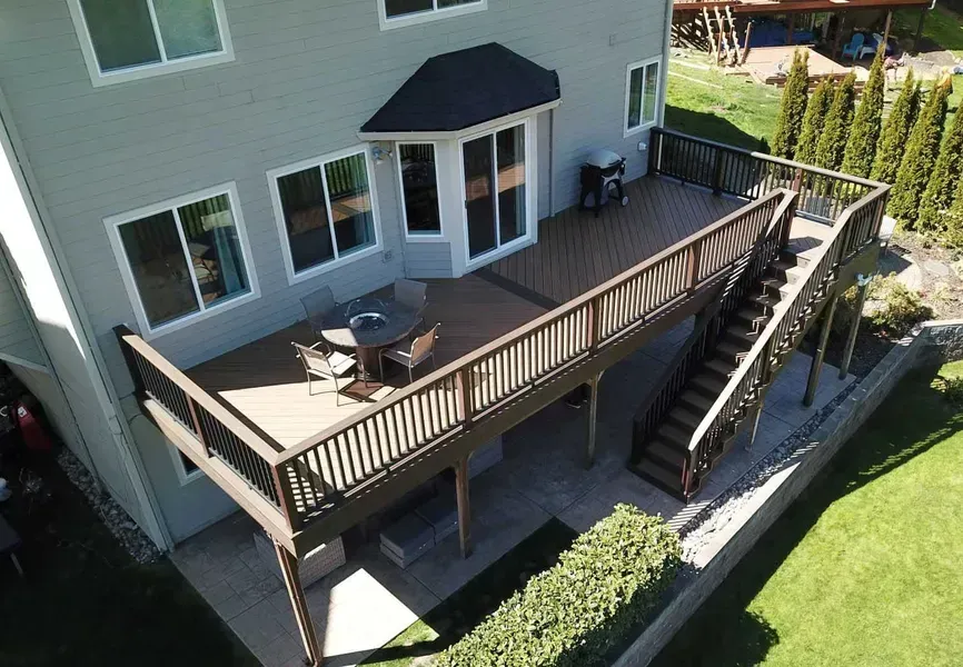 Elevated wooden deck attached to a gray house, with stairs, furniture, and green lawn.