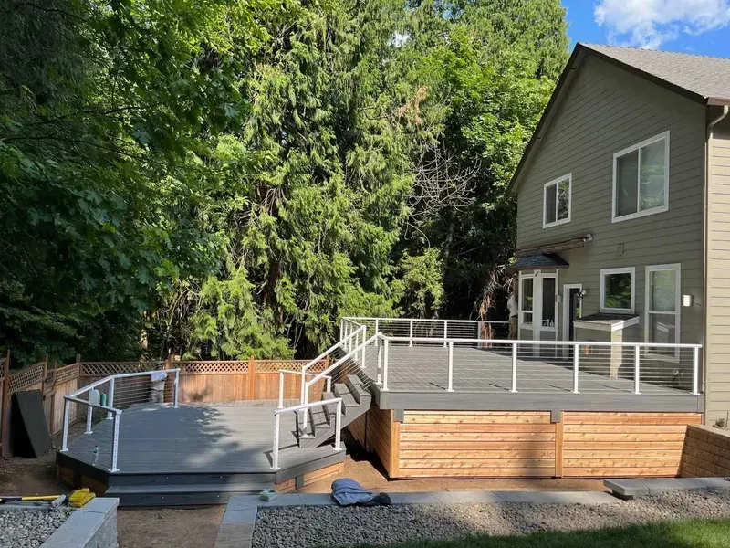 Newly built deck with gray decking, glass railings, and natural wood base, attached to a house.