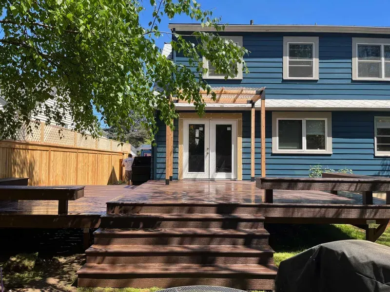 Backyard deck with stairs, built-in benches, and pergola. Blue house with French doors in the background.