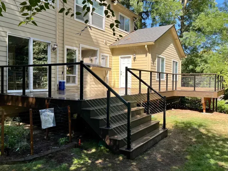 A two-story house with a wooden deck and black cable railing. Steps lead down to the yard.