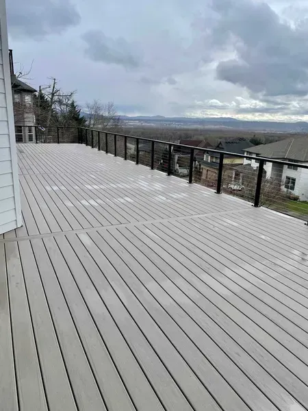 Gray composite deck with black railing overlooking a distant valley under a cloudy sky.