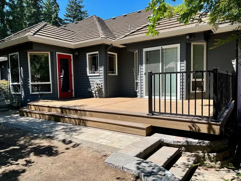 Backyard deck with dark gray house, red door, and black railing.