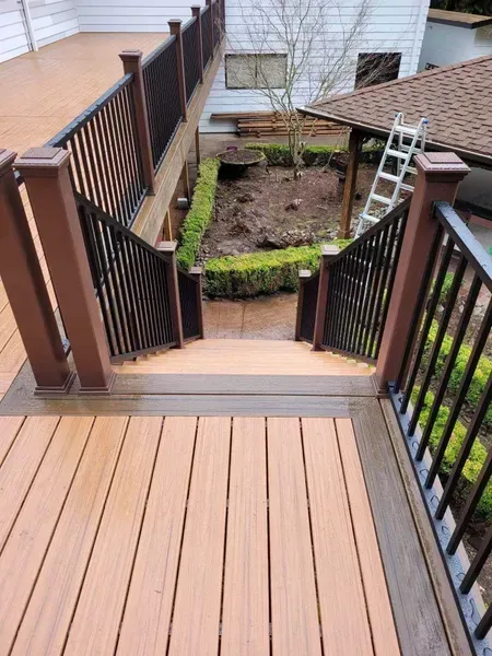 Wooden deck with stairs leading down to a garden area, brown and black railing.